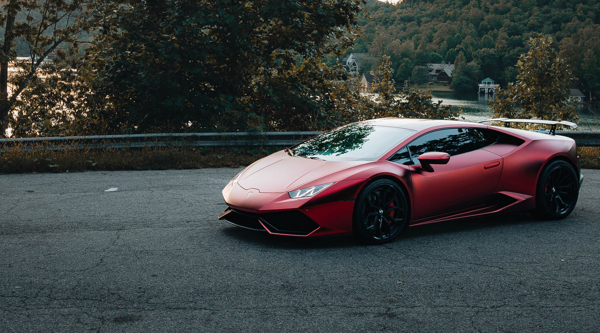 Red Lamborghini with a satin vehicle wrap beside a lake